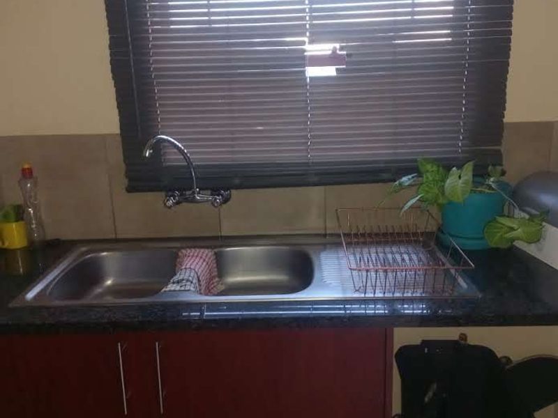 A functional kitchen sink area featuring a double bowl stainless steel sink, granite countertop, and dark wood-look cabinetry with venetian blinds.