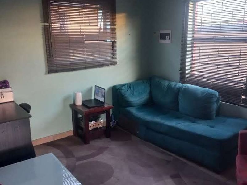 A living room area featuring tiled flooring and venetian blinds on the windows, providing a functional space with natural light.