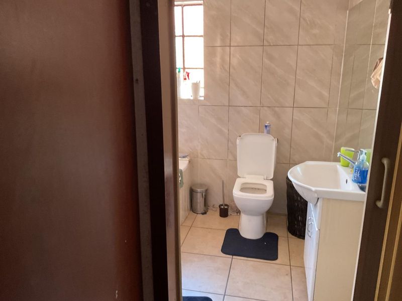 A functional bathroom featuring tiled walls and flooring, equipped with a standard toilet, pedestal basin, and bathtub.