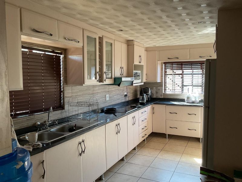 A functional kitchen featuring light-toned built-in cabinetry, dark granite countertops, double basin sink, and tiled flooring with ample natural light.