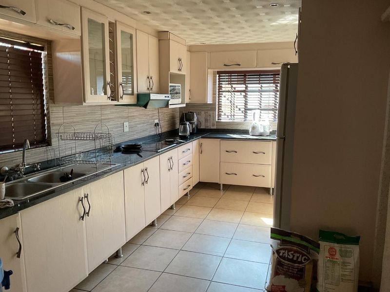 A functional kitchen featuring laminate cabinetry, granite countertops, a double basin sink, and tiled flooring with ample natural light.