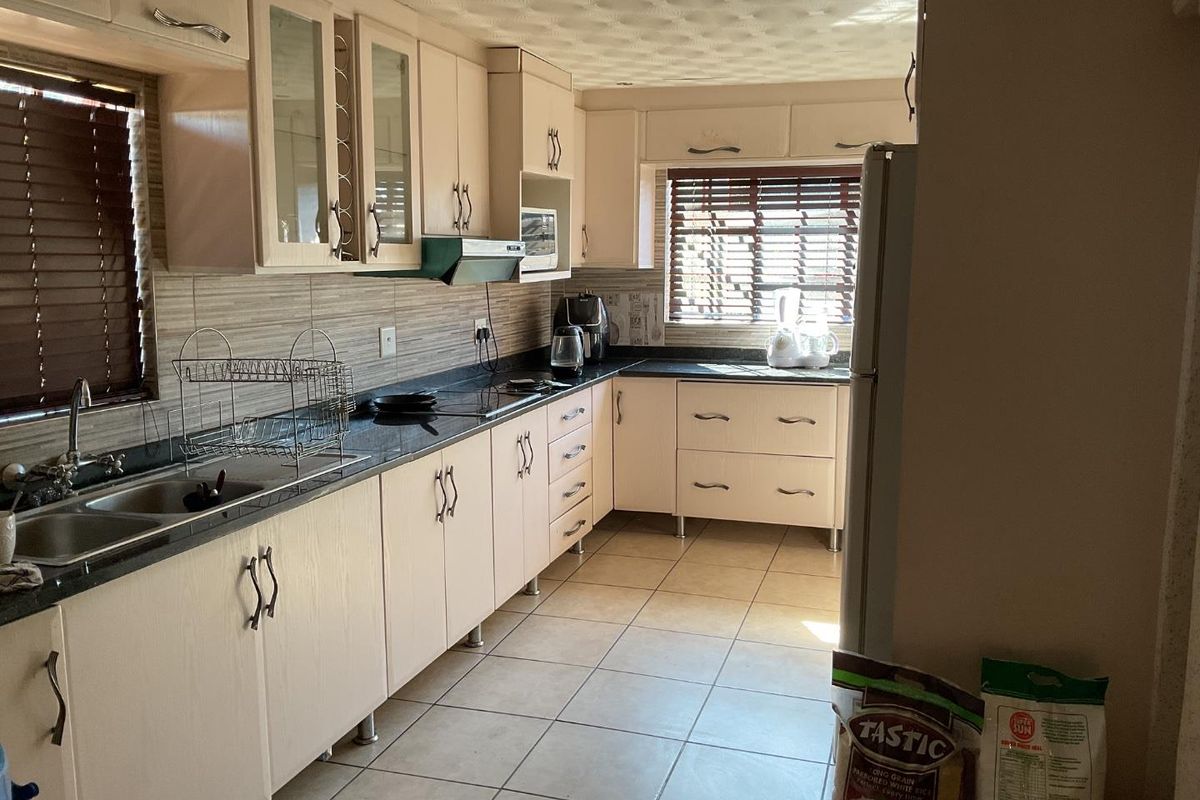 A functional kitchen featuring laminate cabinetry, granite countertops, a double basin sink, and tiled flooring with ample natural light.