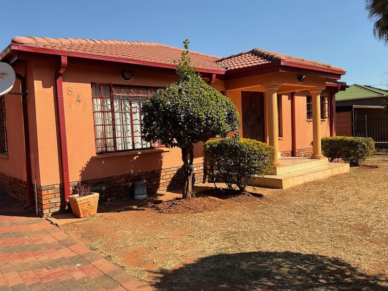 Front elevation of a single-story house featuring a tiled roof, brick accents, concrete columns at the entrance, and a paved driveway.