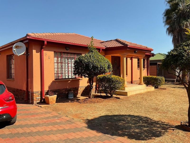 Front elevation of a single-story house featuring a tiled roof, brick base, paved driveway, and a covered entrance porch with decorative columns.