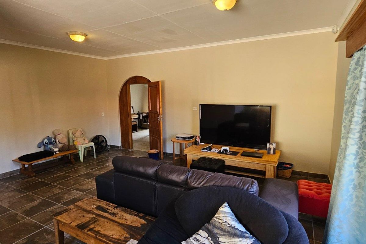 A spacious living room featuring tiled flooring, an arched doorway leading to an adjacent room, and large windows with curtains.