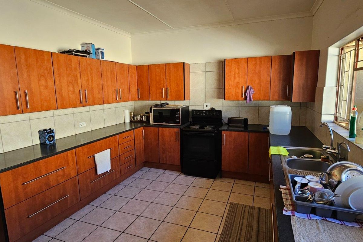 A functional kitchen featuring wood-finish cabinetry, dark countertops, tiled splashbacks, and a built-in stove with an extractor fan.
