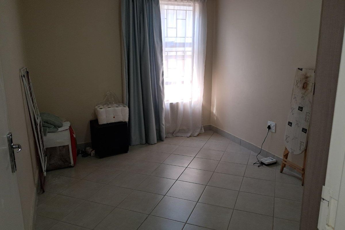 A simple bedroom featuring neutral wall paint, tiled flooring, and a window with curtain tracks.