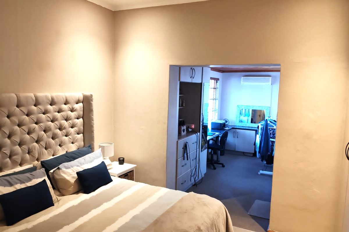 A bedroom featuring neutral walls and recessed lighting, with an adjoining space containing built-in cabinetry and a wall-mounted air conditioning unit.