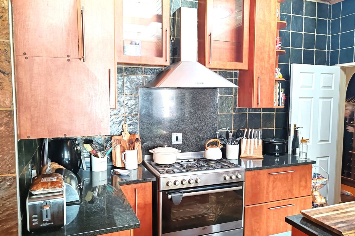 A functional kitchen featuring wooden cabinetry, granite countertops, a stainless steel gas stove with extractor fan, and dark tiled backsplash.