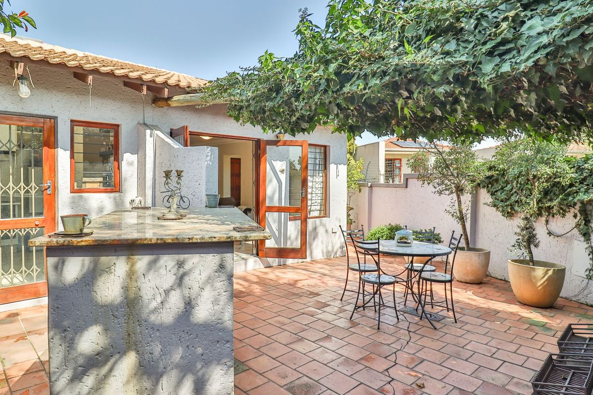 A private rear patio area featuring terracotta tile flooring, a built-in stone-topped counter, and direct access to the interior through wooden doors.