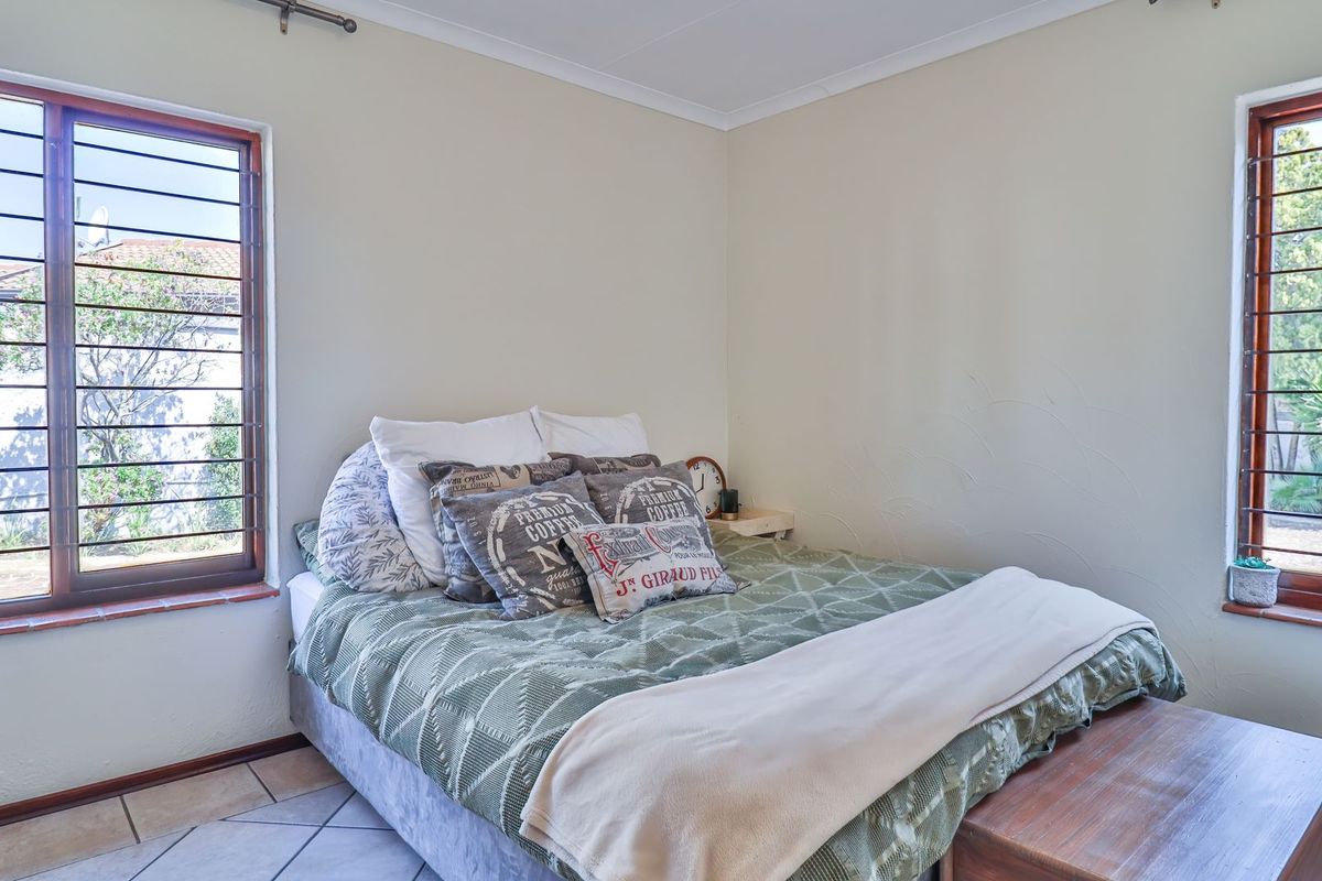 A bedroom featuring tiled flooring and dual windows with security bars, providing natural light and garden views.