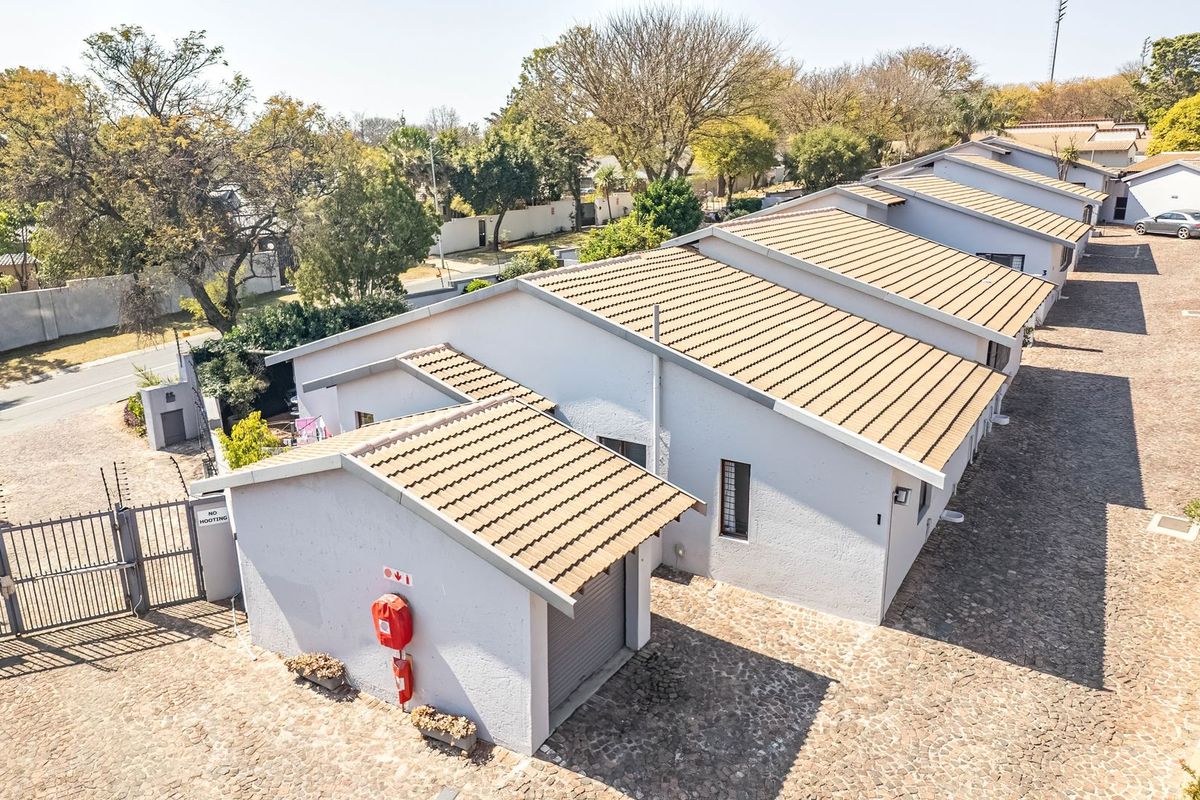 Aerial view of a townhouse complex featuring tiled roofs, paved driveways, and secure perimeter fencing with an access gate.