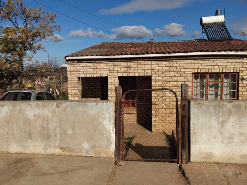 Front view of a face brick house featuring a solar water heater, tiled roof, and a gated entrance with a concrete boundary wall.