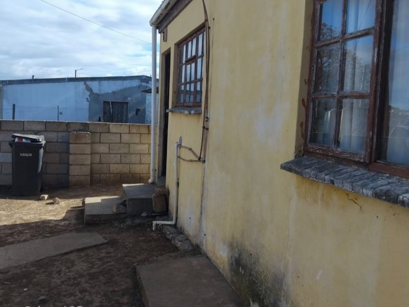 Rear exterior view of the property showing weathered yellow plaster walls, timber-framed windows, and a concrete pathway leading to a boundary wall.