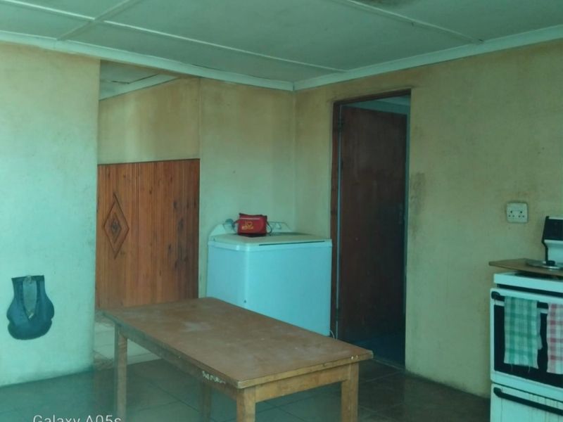 A dated kitchen area featuring tiled floors, timber wall paneling, and a freestanding stove, requiring significant cosmetic updates and ceiling repairs.