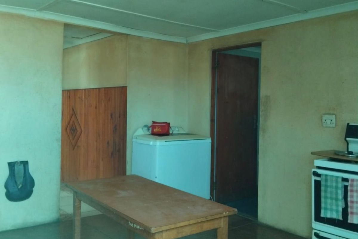 A dated kitchen area featuring tiled floors, timber wall paneling, and a freestanding stove, requiring significant cosmetic updates and ceiling repairs.