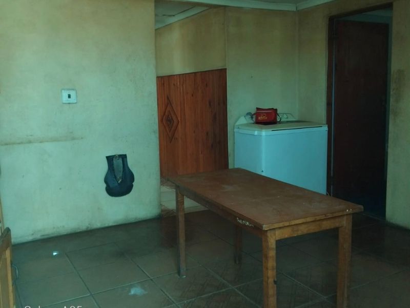A functional laundry area featuring tiled flooring and timber wall paneling, currently in need of cosmetic updates and wall repairs.