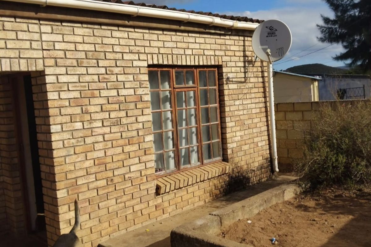 Rear exterior view of a face brick house featuring a solar water heater, satellite dish, and a concrete garden planter.