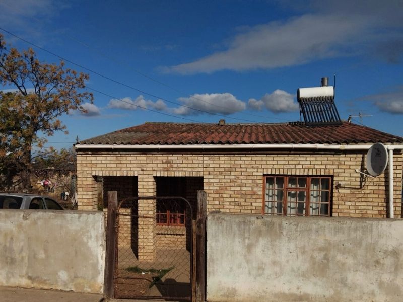 Front view of a face brick house featuring a tiled roof, solar water heater, and a gated concrete boundary wall.