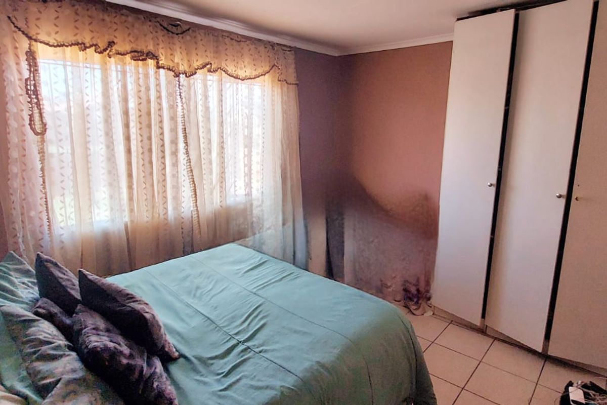 A bedroom featuring built-in cupboards and tiled flooring, currently showing signs of significant wall damage requiring repair.