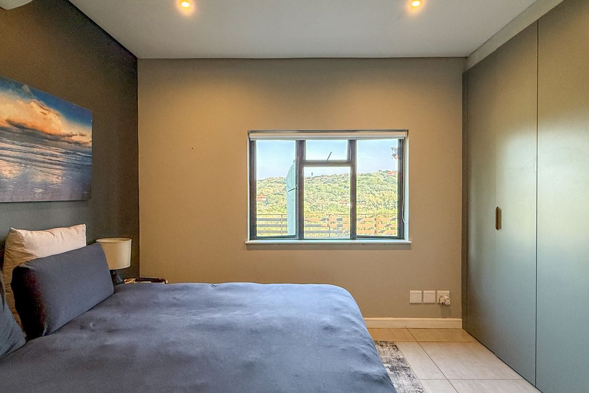 A well-maintained bedroom featuring built-in floor-to-ceiling cabinetry, recessed ceiling lighting, and a window offering scenic hillside views.