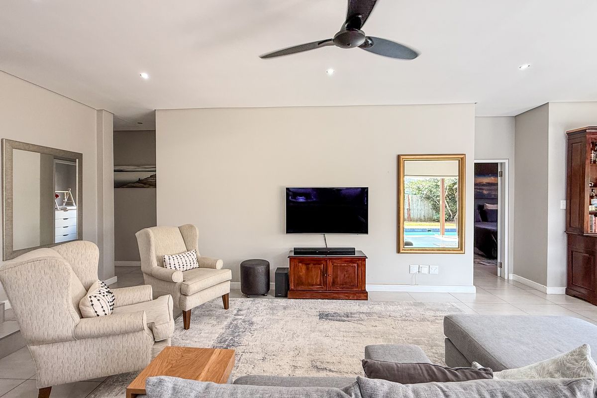 Spacious living room featuring tiled flooring, recessed downlighting, and a ceiling fan, with a clear view through to the outdoor pool area.