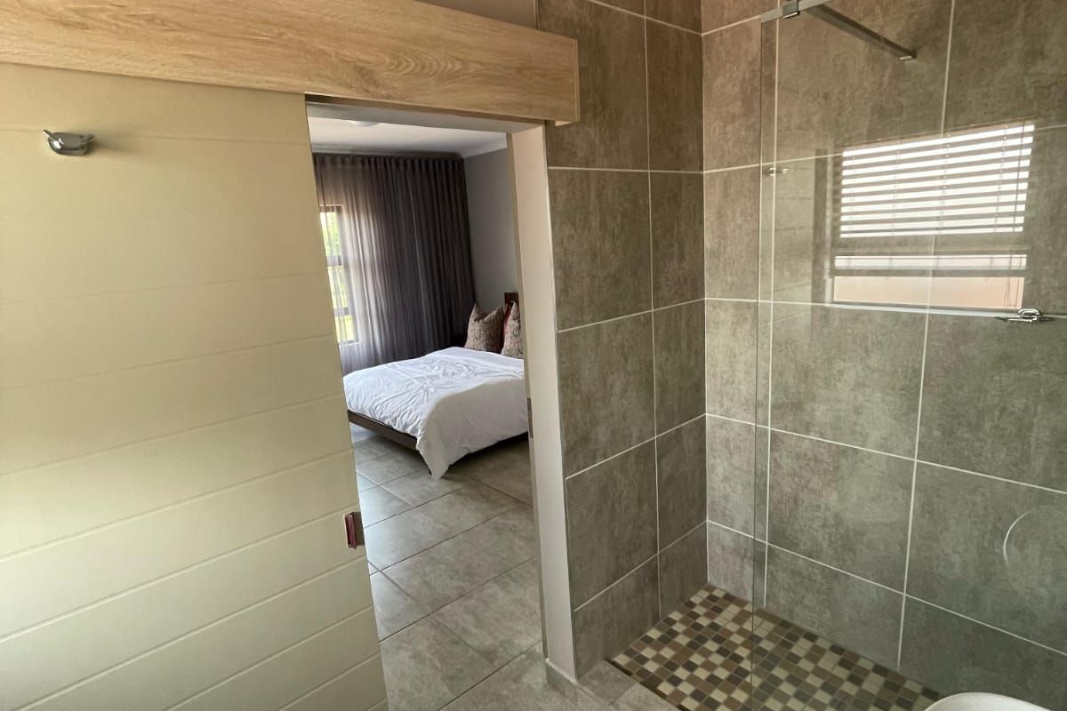 Modern bathroom featuring a glass-enclosed shower with tiled flooring, adjacent to a bedroom accessible via a sliding door.