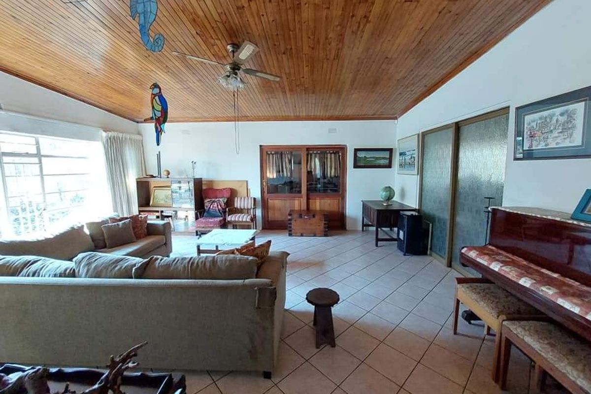 Spacious living room featuring a high timber-clad vaulted ceiling, tiled flooring, and large windows providing ample natural light.
