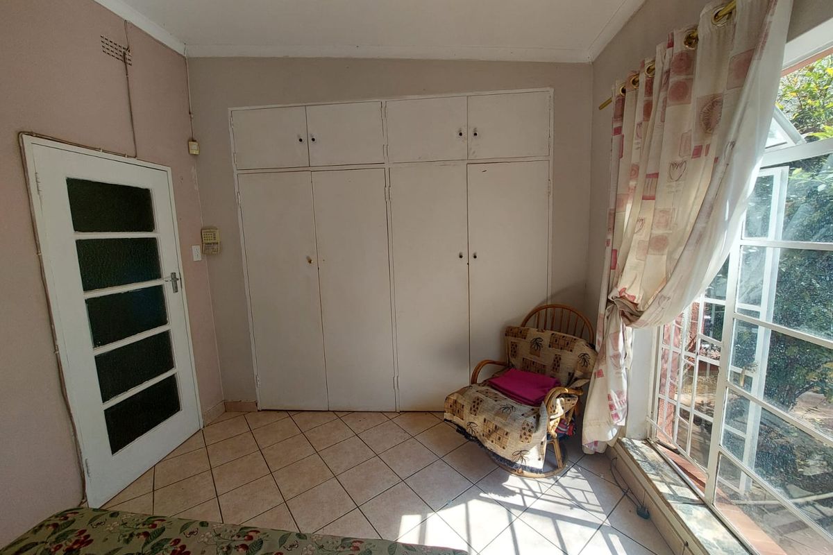 A bedroom featuring built-in cupboards, tiled flooring, and large windows allowing for natural light.
