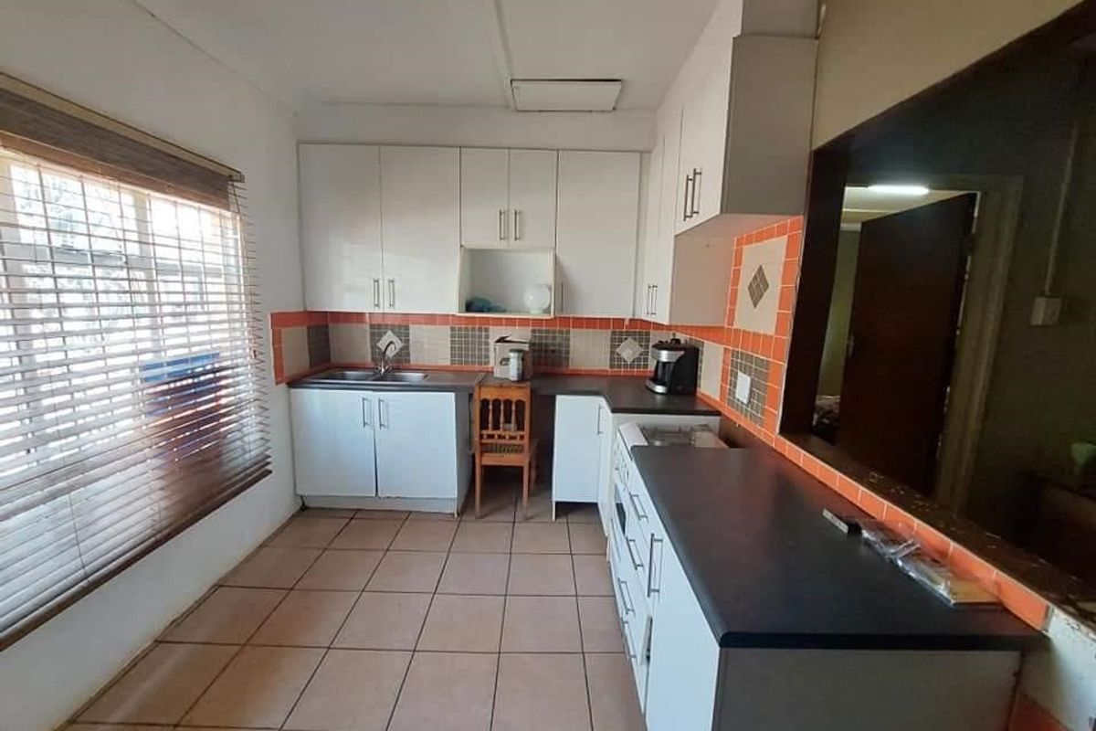 A functional kitchen featuring white cabinetry, dark countertops, tiled flooring, and a pass-through window connecting to the adjacent living space.