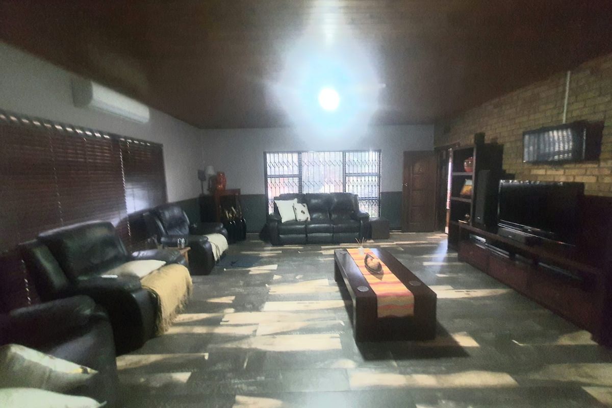 Spacious living room featuring a dark wood-paneled ceiling, exposed brick wall, tiled flooring, and a wall-mounted air conditioning unit.