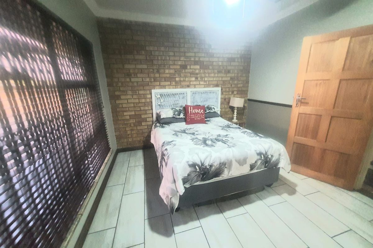 A bedroom featuring a prominent exposed brick feature wall, tiled flooring, and a solid timber door.