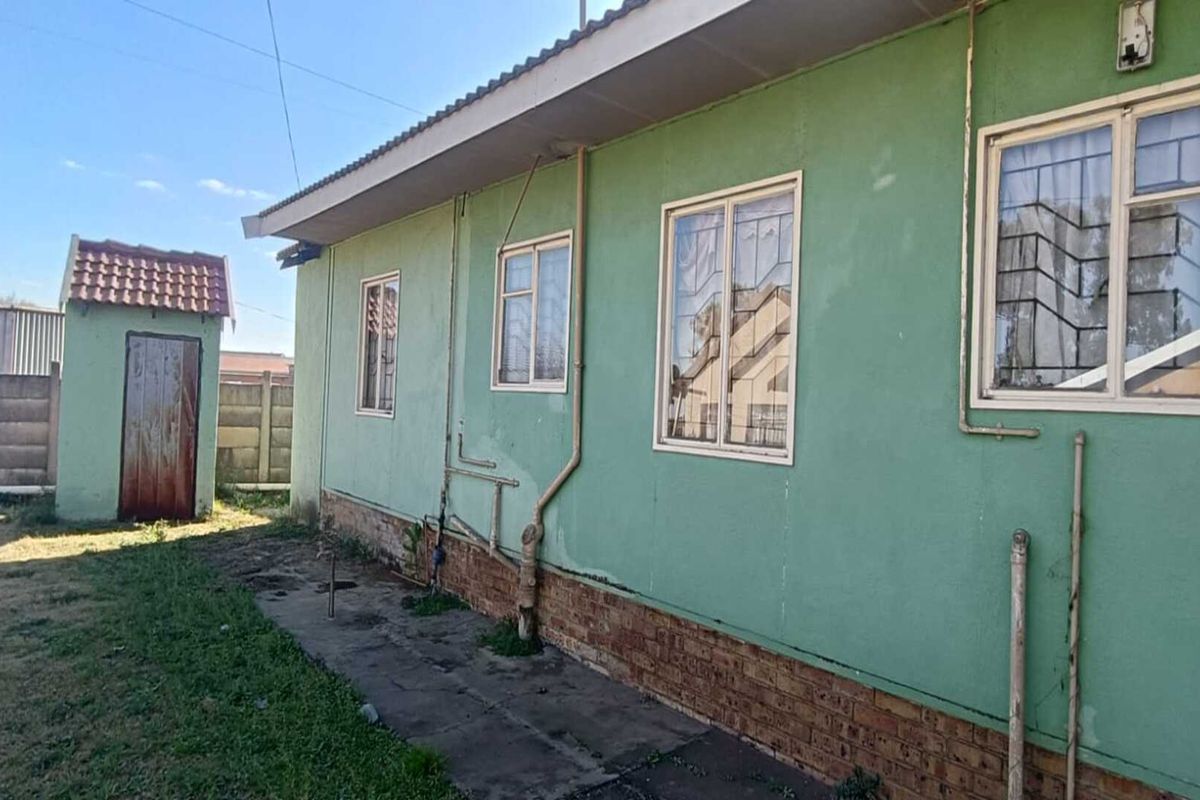 Rear exterior view of the house featuring a green painted facade, exposed plumbing, and a detached outbuilding in the backyard.