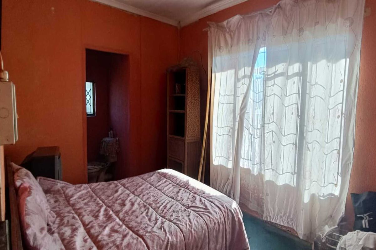 A bedroom featuring an en-suite bathroom, large window with natural light, and dated wall finishes.