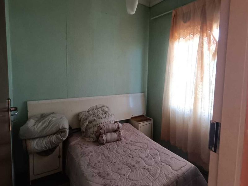A compact bedroom featuring a built-in headboard and a window with security bars, offering a functional space in need of cosmetic updates.