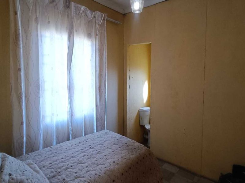 A bedroom featuring a compact en-suite toilet area, requiring cosmetic updates to modernize the wall finishes and overall aesthetic.