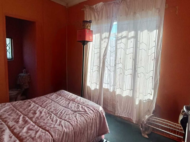 A bedroom featuring an en-suite bathroom and a sliding door leading to the exterior, requiring cosmetic updates to modernize the space.