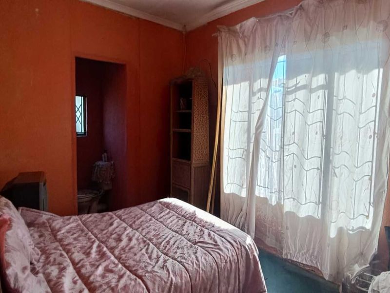 A bedroom featuring an en-suite bathroom and a large window, requiring cosmetic updates to the wall finishes and general maintenance.