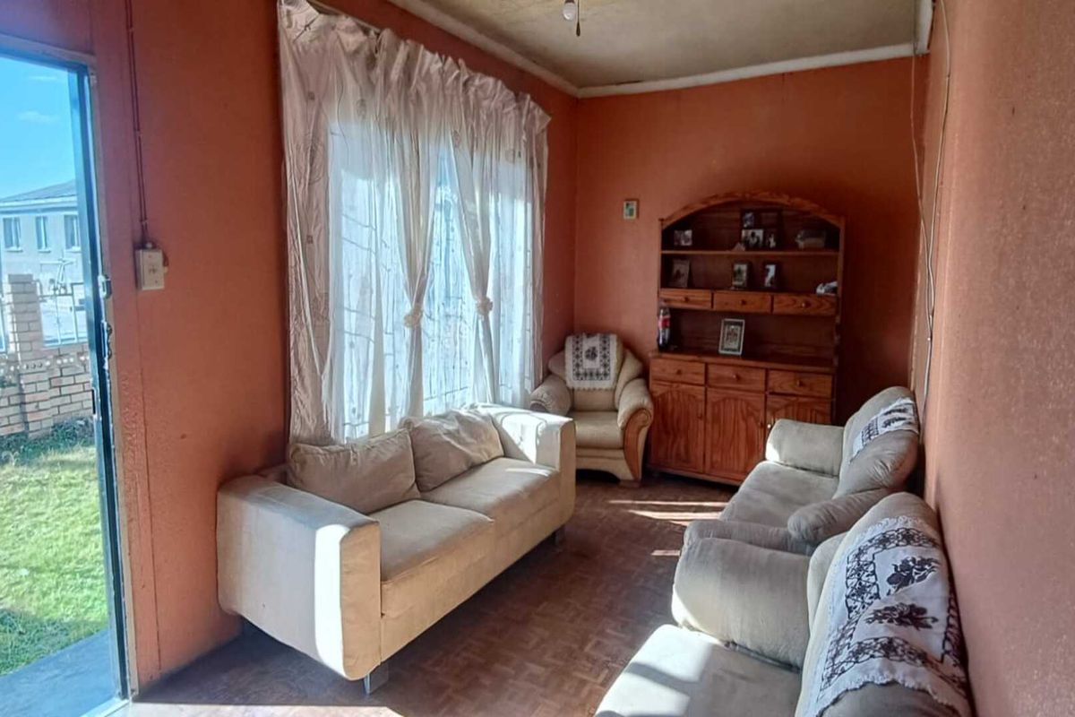 A living room featuring parquet flooring and a sliding glass door providing access to the garden, with dated wall finishes.