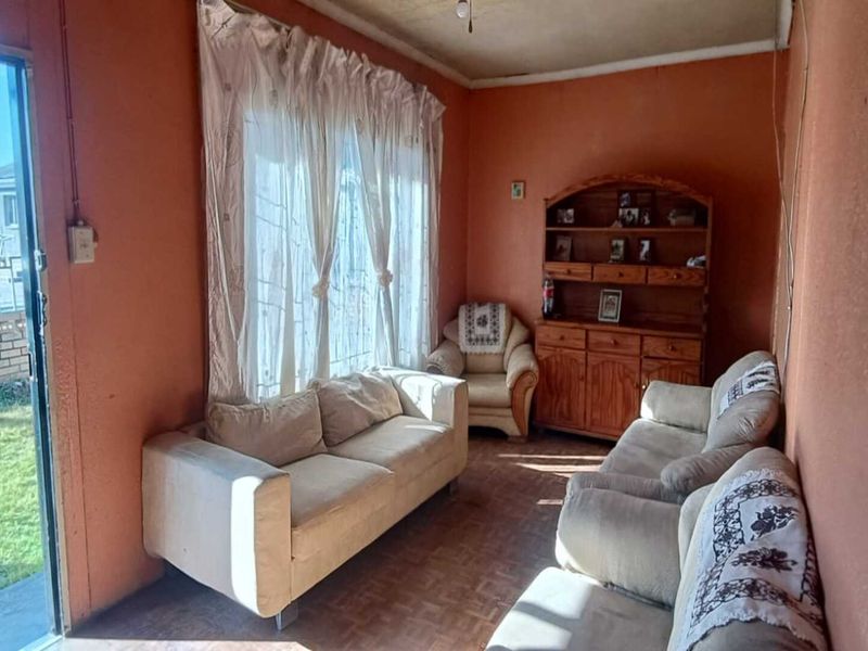 A living room featuring parquet flooring and a sliding glass door providing access to the garden, with dated wall finishes.