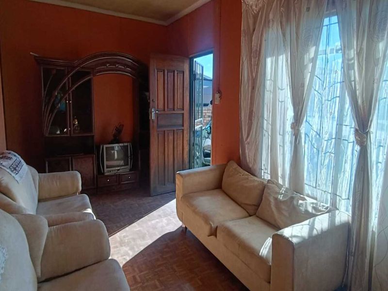 A living room featuring parquet flooring, a timber door with security gate, and large windows allowing natural light.