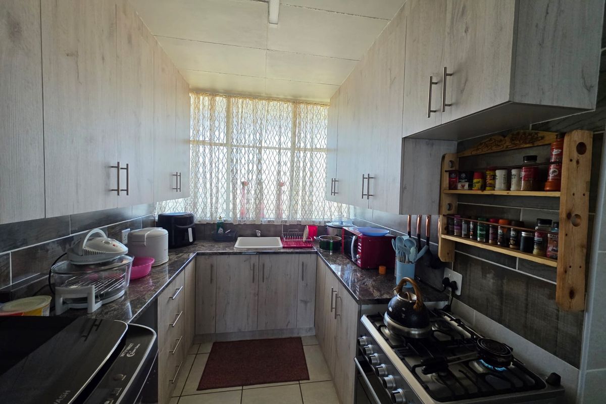 A functional galley-style kitchen featuring light wood-grain cabinetry, granite-look countertops, tiled backsplash, and a gas stove.