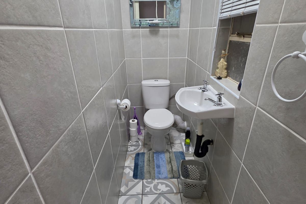 A compact guest bathroom featuring floor-to-ceiling wall tiles, patterned floor tiles, a wall-mounted basin, and a standard toilet.