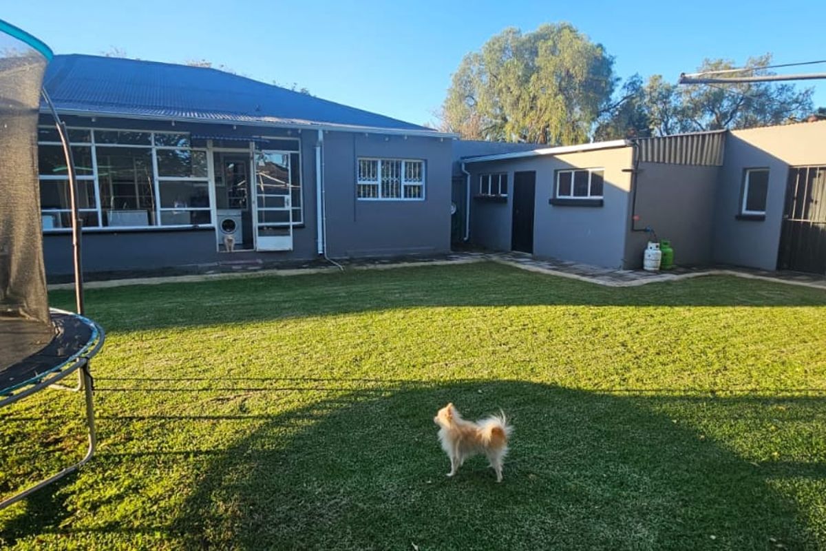 A spacious rear garden featuring a well-maintained lawn, paved pathways, and direct access to the main house and secondary structure.