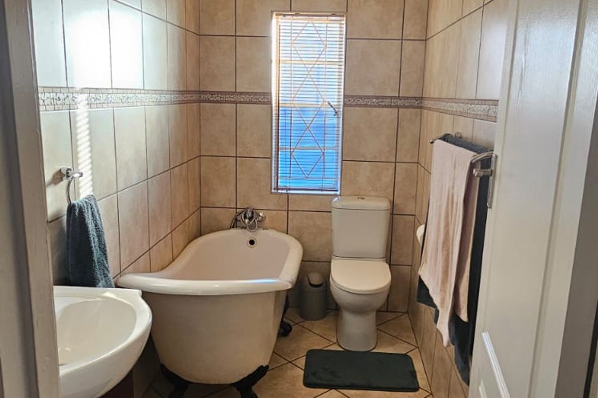A compact bathroom featuring a classic clawfoot bathtub, pedestal vanity, and toilet, finished with neutral floor-to-ceiling ceramic tiling.