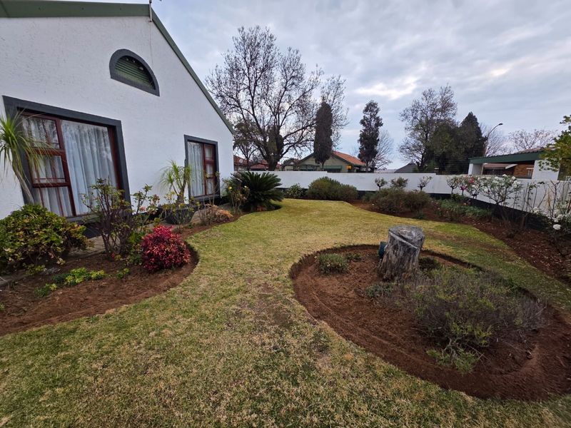 A private rear garden featuring a landscaped lawn, established garden beds, and a boundary wall, providing a quiet outdoor space for the townhouse.