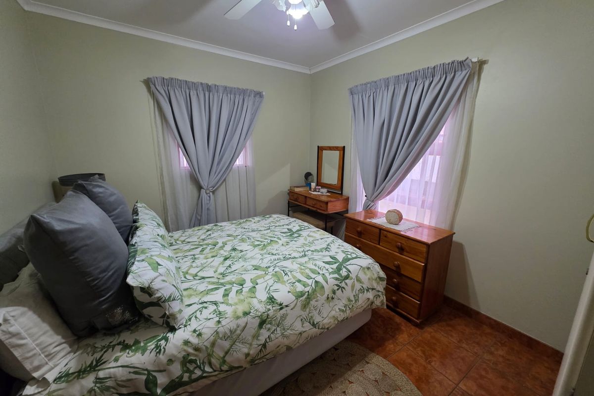 A cozy bedroom featuring tiled flooring, a ceiling fan, and dual windows with curtains, offering a comfortable and functional living space.