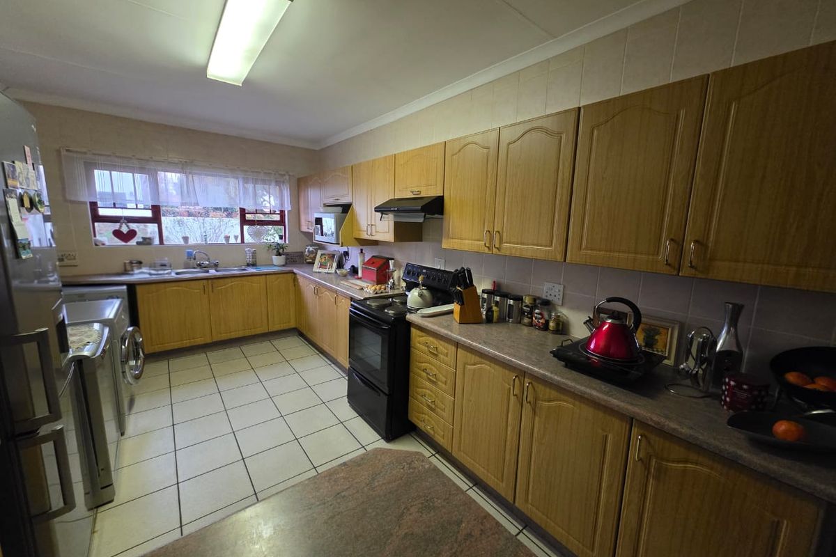 A functional kitchen featuring wood-look cabinetry, tiled flooring, a built-in oven with extractor fan, and ample counter space with a tiled backsplash.