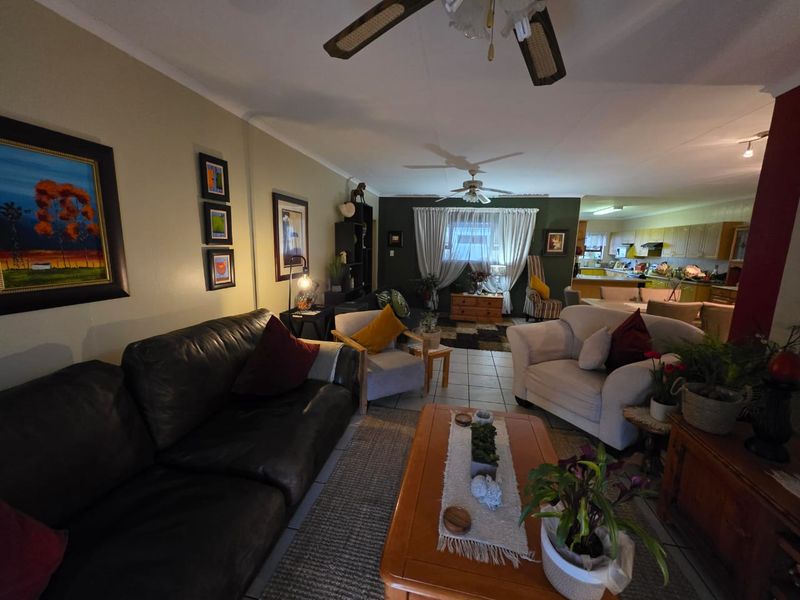 Spacious open-plan living area featuring tiled flooring, ceiling fans, and a connected kitchen with cabinetry, offering a functional and versatile layout.