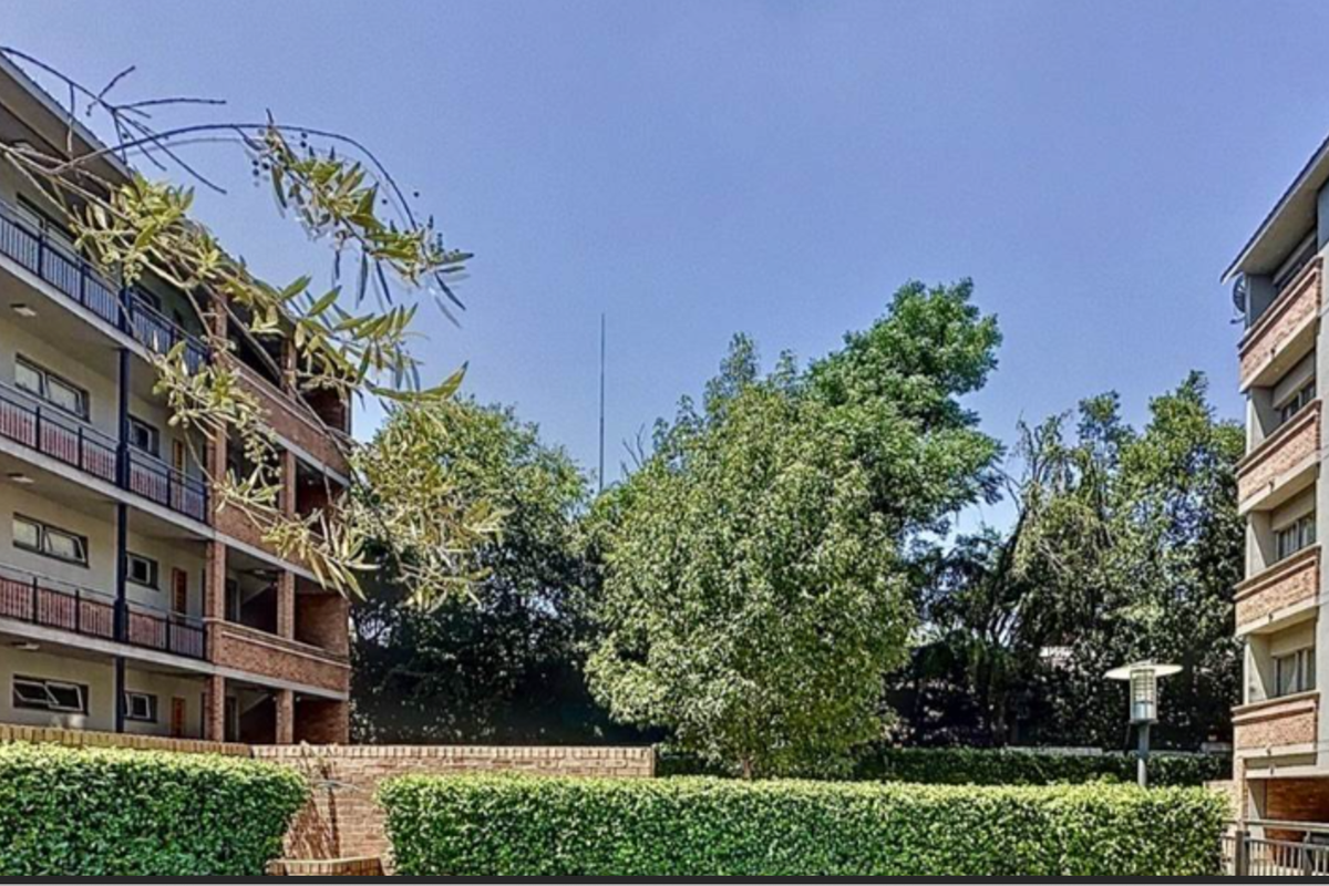 Exterior view of the apartment complex featuring multi-story brick and concrete facades with balconies and landscaped garden areas.